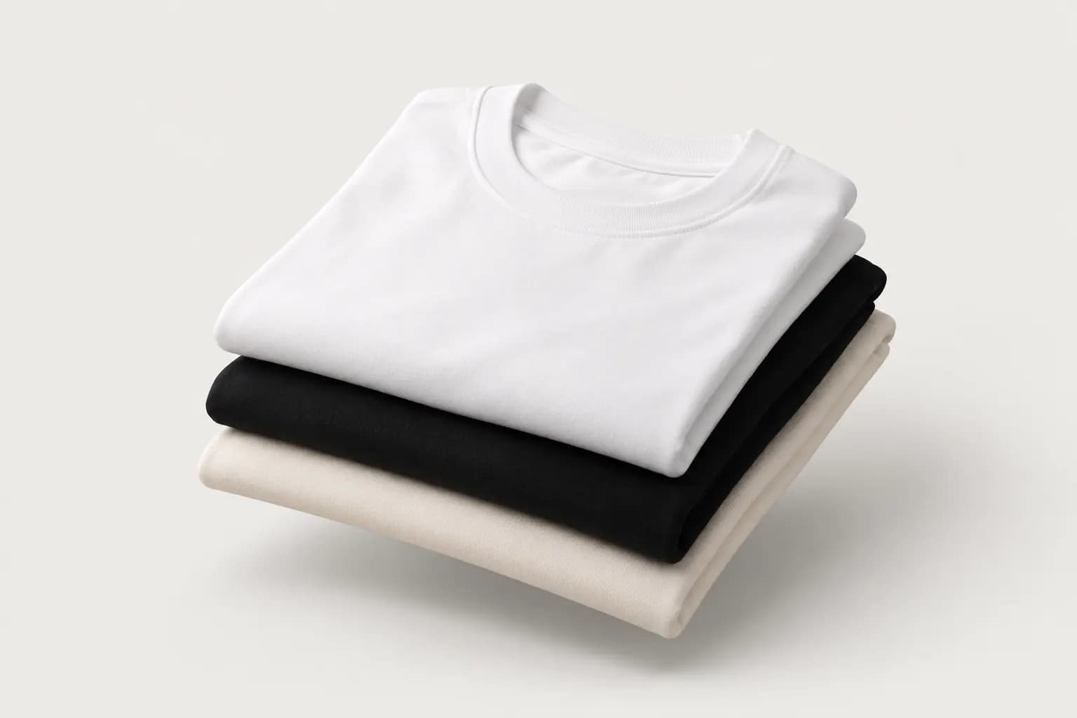 Stack of folded white, black and cream crew neck t-shirts
